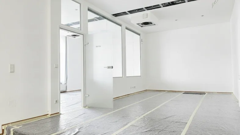 Heller Büroraum im Rohbau mit Glasabtrennung und vorbereitetem Bodenbelag für zukünftige Nutzung.