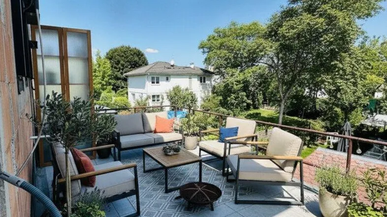Geräumige Terrasse mit modernen Outdoor-Möbeln, Pflanzen und Blick ins Grüne unter blauem Himmel.