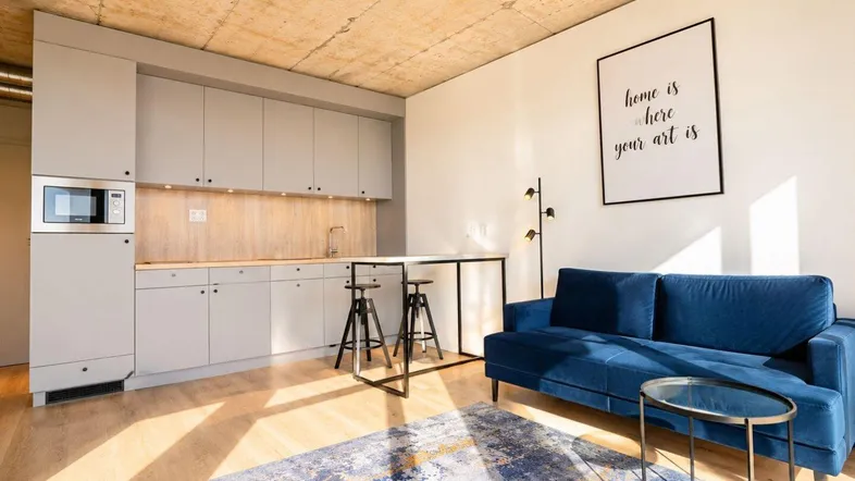 Modernes Studio-Apartment mit integrierter Küchenzeile, Holzboden und gemütlichem blauen Sofa.