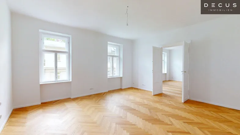 Helles, leeres Zimmer mit Fischgrätparkett und hohen Fenstern, bereit zur individuellen Gestaltung.