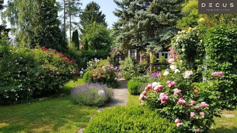 Wunderschöner, gepflegter Garten mit vielfältigen Blumenbeeten, Rosen und einem charmanten Gartenweg.