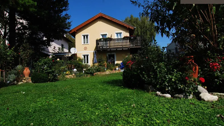 Gelbes Einfamilienhaus mit Satteldach, Balkon und gepflegtem Vorgarten unter blauem Himmel.