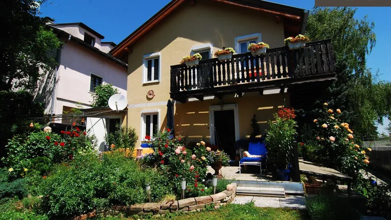 Charmantes Haus mit blühendem Vorgarten und Balkon, ideal für entspannte Stunden im Freien.
