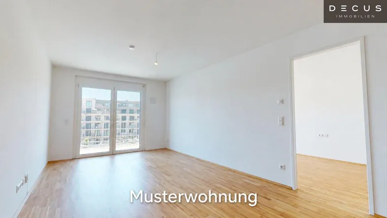 Helles, leeres Wohnzimmer mit Holzboden und Zugang zu einem Balkon oder einer Terrasse.