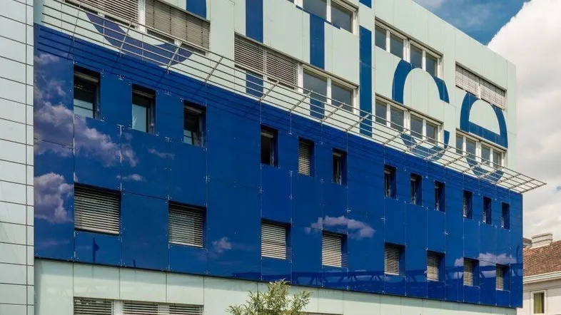 Modernes Bürogebäude mit blauer und weißer Fassade unter einem bewölkten Himmel.