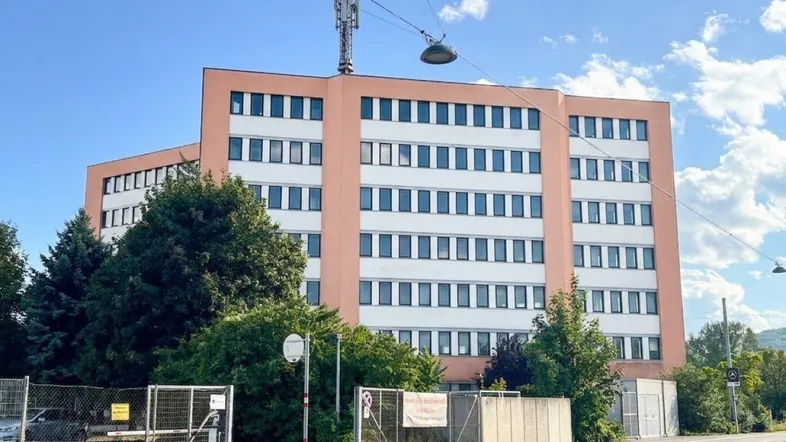 Mehrstöckiges Gebäude mit helloranger Fassade und vielen Fenstern, umgeben von Bäumen und einer Straße.