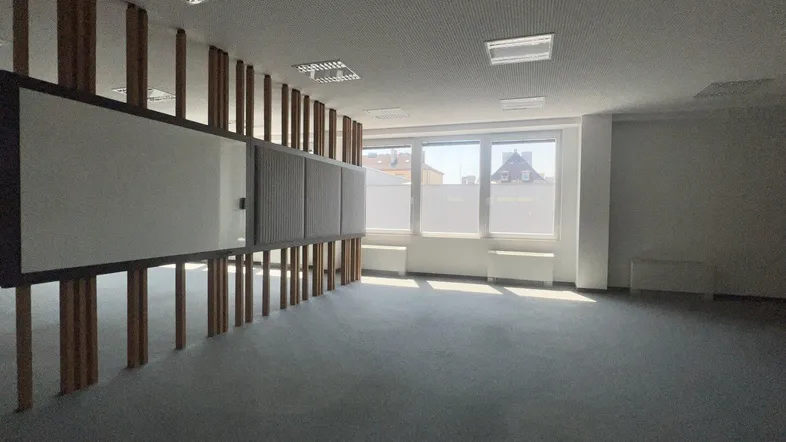 Großer, heller Büroraum mit Teppichboden, vielen Fenstern und einer Trennwandstruktur.