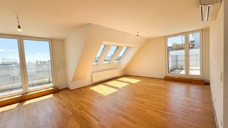 Helles Wohnzimmer mit Holzboden, Dachschrägen und Zugang zu zwei Terrassen.