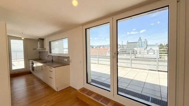 Heller offener Wohn-Essbereich mit integrierter Küche, Parkettboden und Zugang zu einer großen Terrasse.