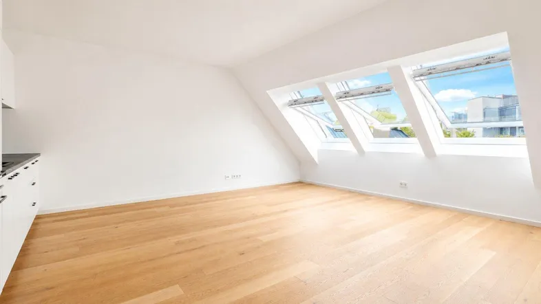 Helles Zimmer mit Holzboden, Dachschrägen und großen Dachfenstern, ideal als Wohn- oder Schlafbereich.