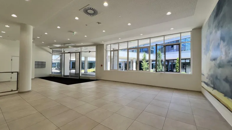 Geräumige und helle Bürolobby mit großen Fenstern, modernem Fliesenboden und viel Tageslicht.