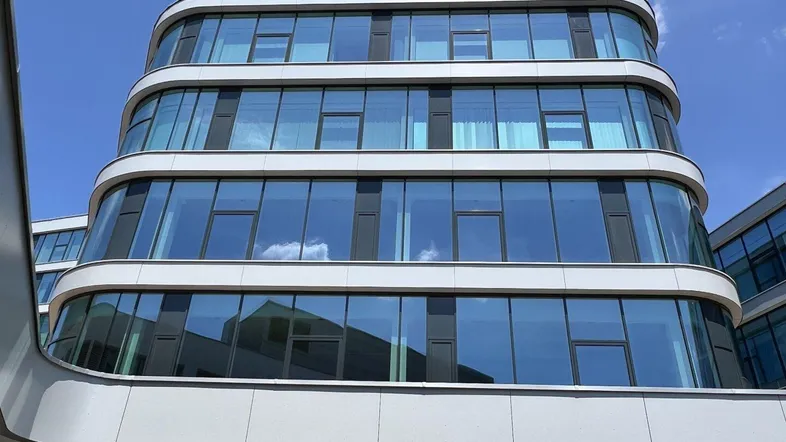 Moderne Bürogebäude-Fassade mit geschwungenen Linien und reflektierenden Glasflächen unter blauem Himmel.