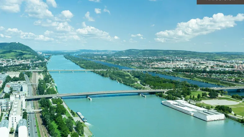 Luftaufnahme mit weitem Blick über den Fluss, Brücken und die umliegende Stadtlandschaft unter blauem Himmel.