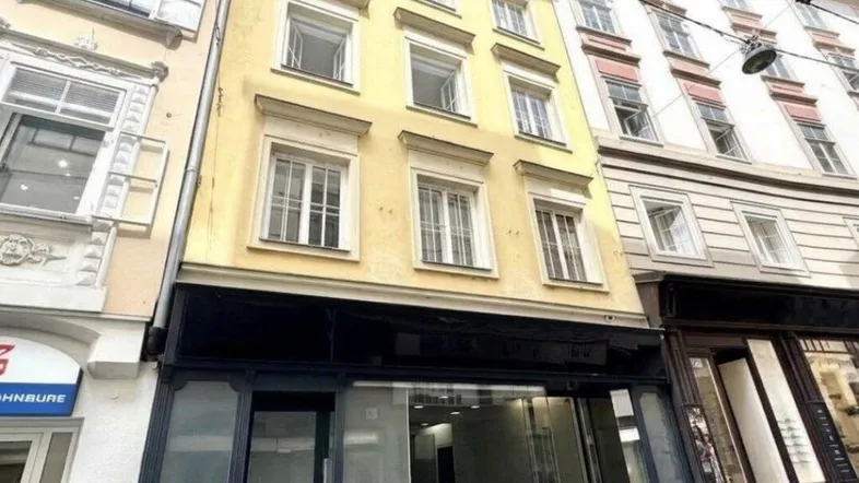 Historisches Gebäude mit gelber Fassade und Ladenlokal im Erdgeschoss in urbaner Umgebung.