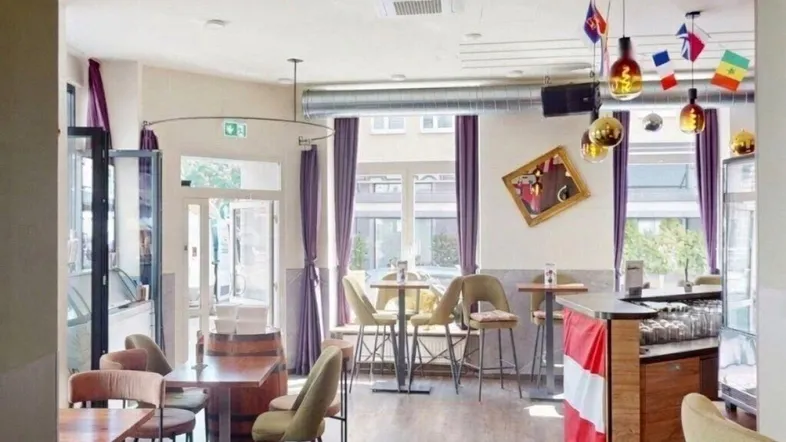 Gemütlicher Innenbereich eines Restaurants oder einer Bar mit Tischen, Stühlen und einer Theke, dekoriert mit Flaggen.