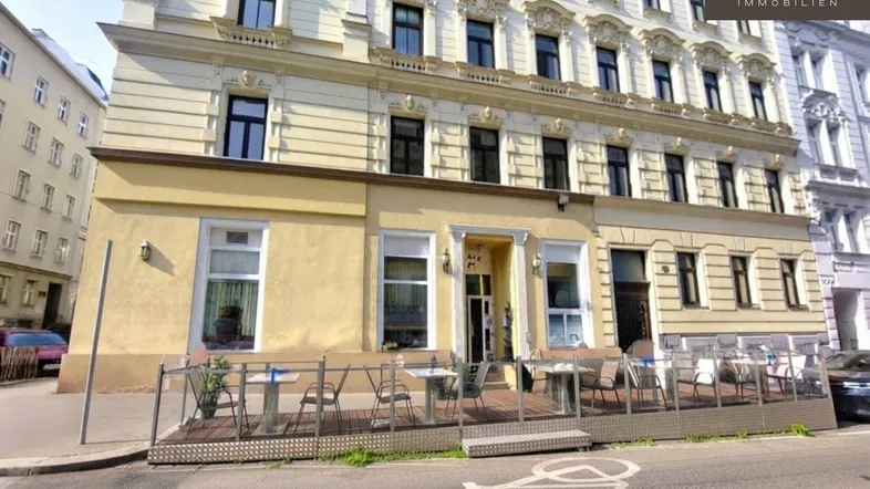 Gebäudefassade mit einem charmanten Außenbereich und Tischen für Gäste an der Straße.