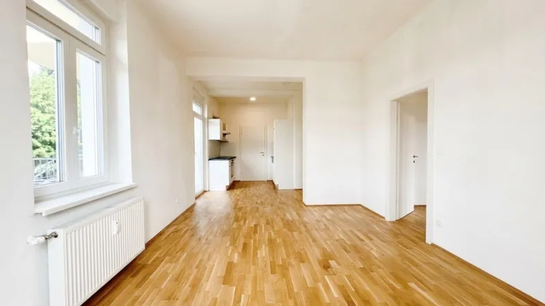 Helles Wohnzimmer mit Parkettboden, großen Fenstern und integrierter Küchenzeile.