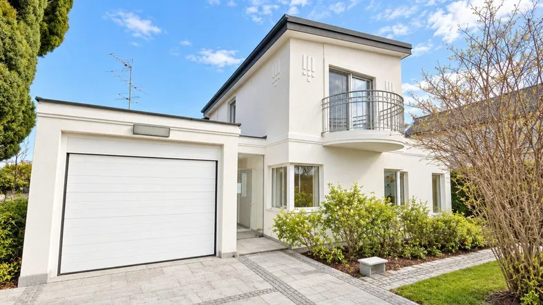 Modernes Einfamilienhaus mit weißer Fassade, integrierter Garage und gepflasterter Auffahrt.