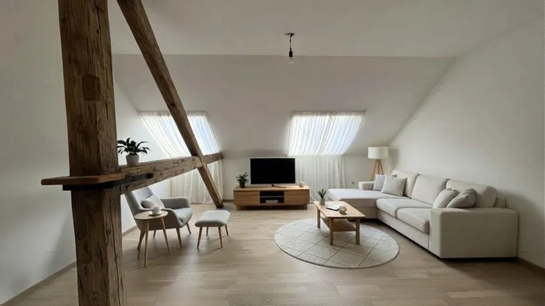 Helles Wohnzimmer im Dachgeschoss mit sichtbaren Holzbalken, Dachfenstern und modernem Sofa.