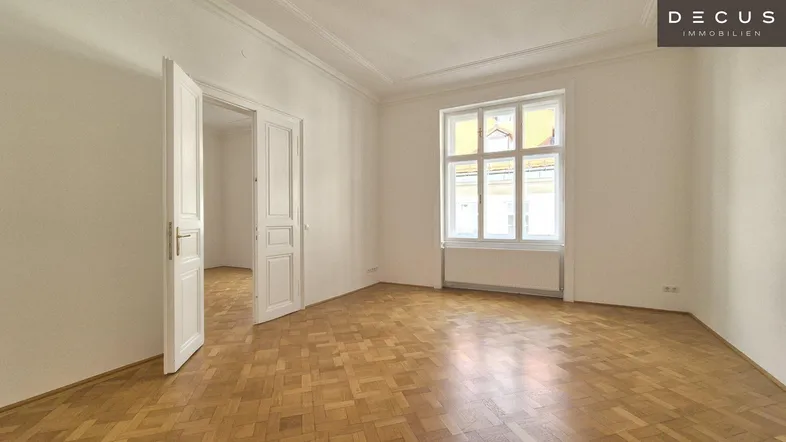 Helles Zimmer mit Fischgrätparkett und hohen Fenstern, bereit zur individuellen Gestaltung.