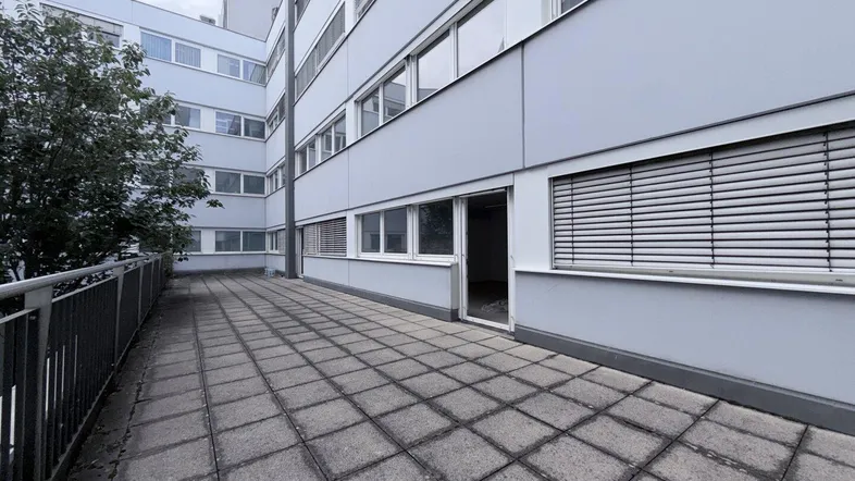 Große gepflasterte Terrasse mit Blick auf die Gebäudefassade und Fenster mit Jalousien.