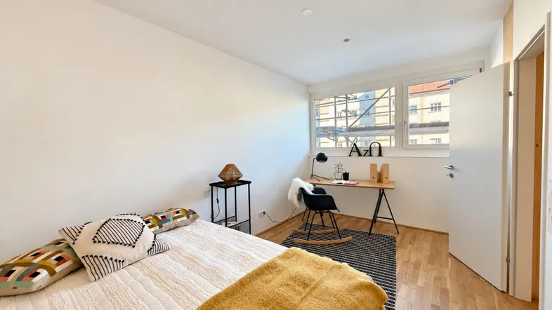 Helles Schlafzimmer mit Holzboden, einem Arbeitsbereich und Blick auf die Baustelle.