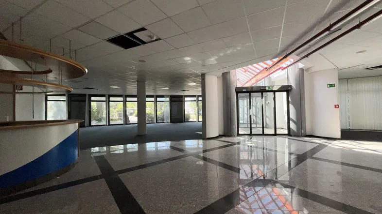 Großer, offener Gewerberaum mit Empfangsbereich, glänzendem Fliesenboden und viel Tageslicht durch die Glasfassade.