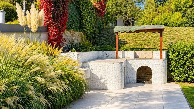 Großzügige Terrasse mit integriertem Grillbereich, umgeben von üppiger Bepflanzung und Bäumen.