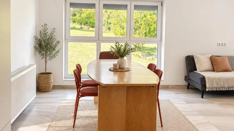 Heller Essbereich mit Holztisch, roten Stühlen und Blick ins Grüne durch große Fenster.