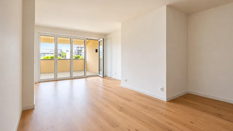 Helles, leeres Wohnzimmer mit Holzboden und Zugang zu einem sonnigen Balkon, ideal für Neubau.
