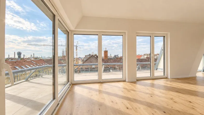 Helles, leeres Zimmer mit Holzboden und großen Fenstern, die einen weiten Stadtblick bieten.
