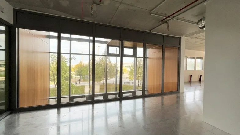 Großer, leerer Raum mit hohen Fenstern, Blick ins Grüne und sichtbaren Installationen an der Decke.