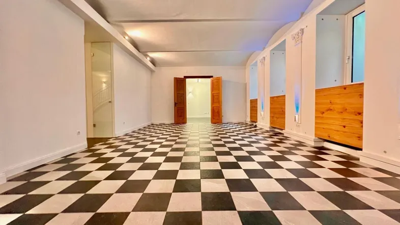 Großer, heller Raum mit markantem schwarz-weißem Schachbrettmuster-Boden und dekorativen Säulen.