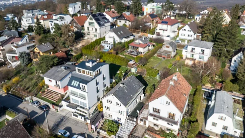 Luftaufnahme einer Wohnsiedlung mit vielen Häusern und grüner Umgebung in hügeliger Landschaft.