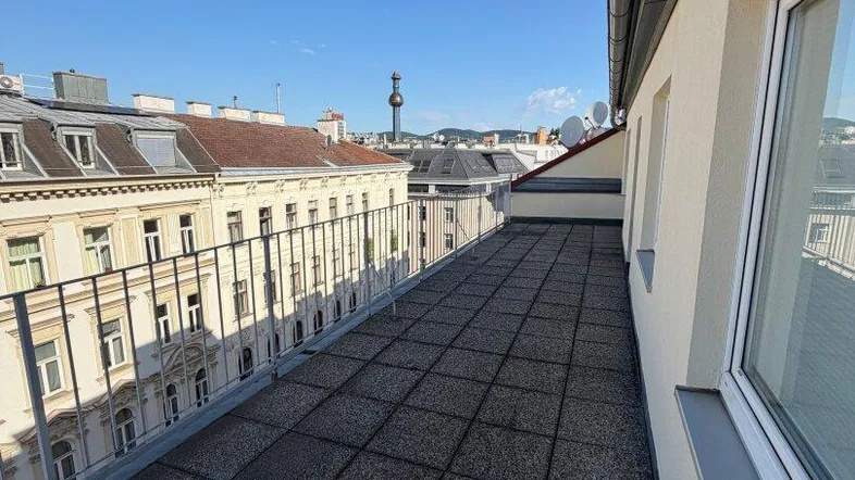 Große Dachterrasse mit Fliesenboden und weitem Blick über die Stadt unter blauem Himmel.