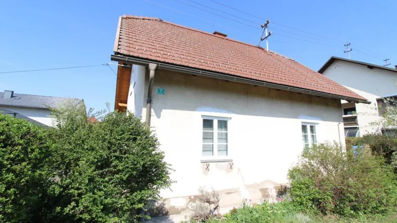 Seitenansicht eines Hauses mit Ziegeldach und grünen Büschen im Vordergrund.