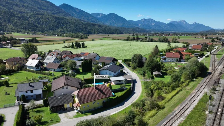 Luftaufnahme eines Wohngebiets mit Häusern, Feldern und Bergen im Hintergrund, die Immobilie ist markiert.