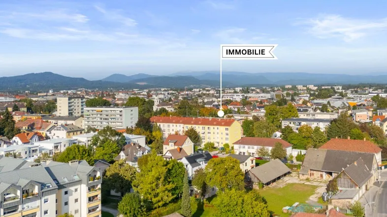 Luftaufnahme der Stadt mit Bergen im Hintergrund und markierter Immobilienlage.