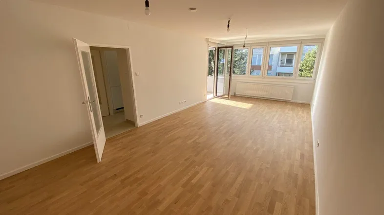 Helles und geräumiges Wohnzimmer mit Parkettboden und großen Fenstern, die viel Tageslicht hereinlassen.