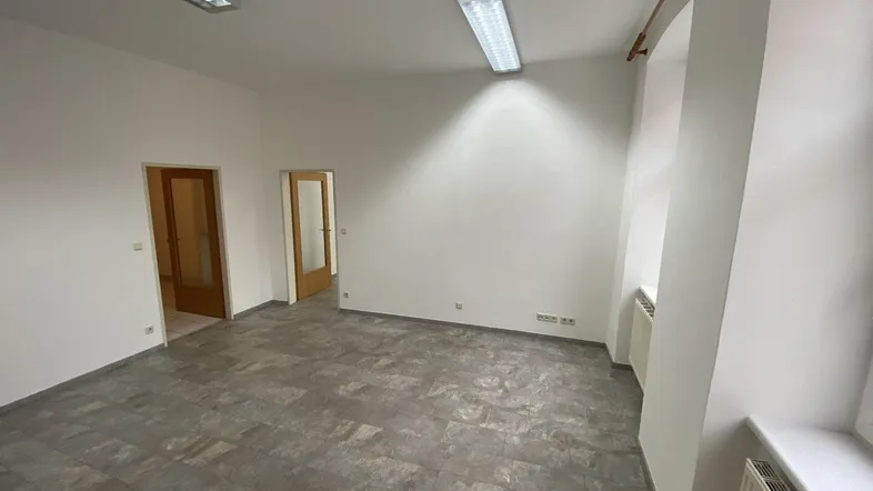 Geräumiger, leerer Büroraum mit grauem Vinylboden, weißen Wänden und zwei Türen.