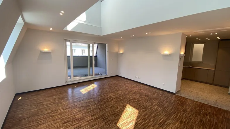 Helles Wohnzimmer mit Parkettboden, Dachschrägen und Zugang zu einem Balkon.