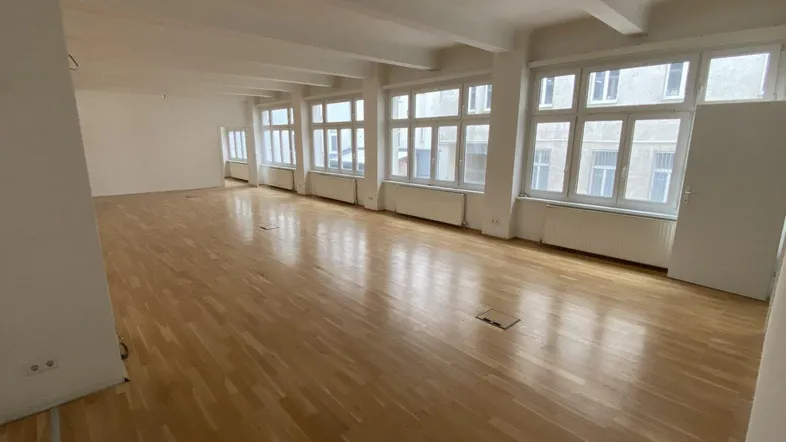 Großer, heller Büroraum mit vielen Fenstern und hellem Holzparkettboden, ideal für offene Arbeitsbereiche.