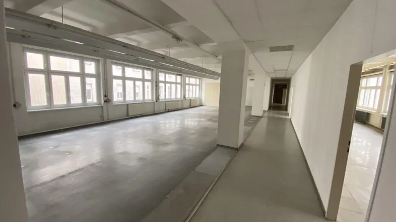 Großer, heller Büroraum mit vielen Fenstern und Betonboden, ideal für flexible Arbeitsplatzgestaltung.