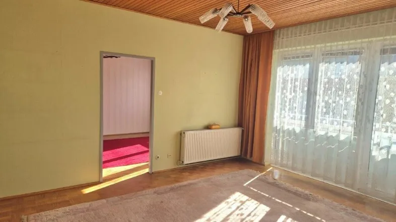 Helles Wohnzimmer mit Parkettboden, Holzdecke und Blick nach draußen durch große Fenster.