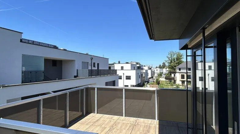 Geräumiger Balkon mit Holzboden und Blick auf moderne Gebäude unter blauem Himmel.