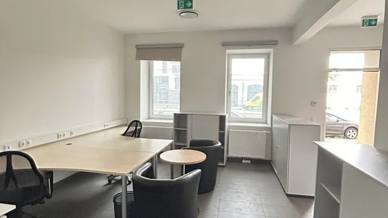 Heller Büroraum mit mehreren Arbeitsplätzen, Schränken und Fenstern, die Tageslicht hereinlassen.