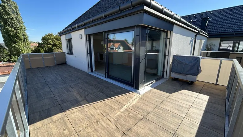 Große Dachterrasse mit Holzfliesen und Blick auf die Umgebung unter blauem Himmel.