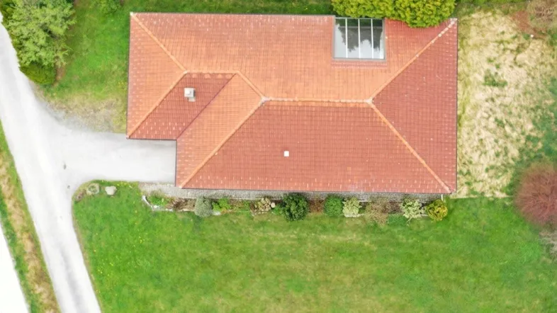 Luftaufnahme eines Einfamilienhauses mit rotem Ziegeldach, umgeben von einem gepflegten Garten.