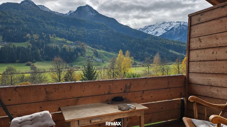 Rustikaler Holzbalkon mit Tisch und Stühlen bietet einen weiten Blick auf die umliegende Berglandschaft.