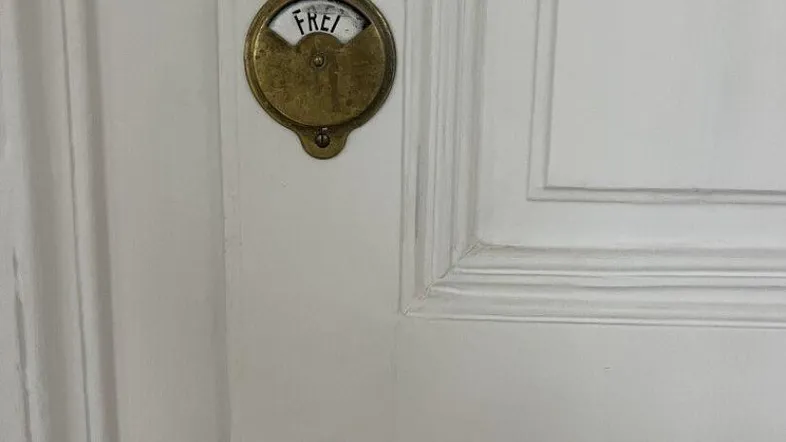 Nahaufnahme einer weißen Tür mit einem antiken Messinggriff und einem 'FREI'-Schild, das den Zustand anzeigt.